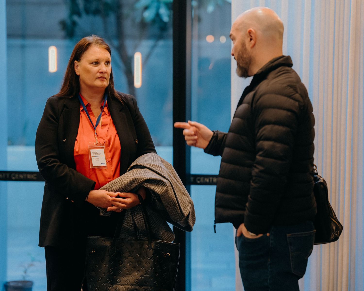 People in business attire networking and mingling at a professional conference event near large windows.