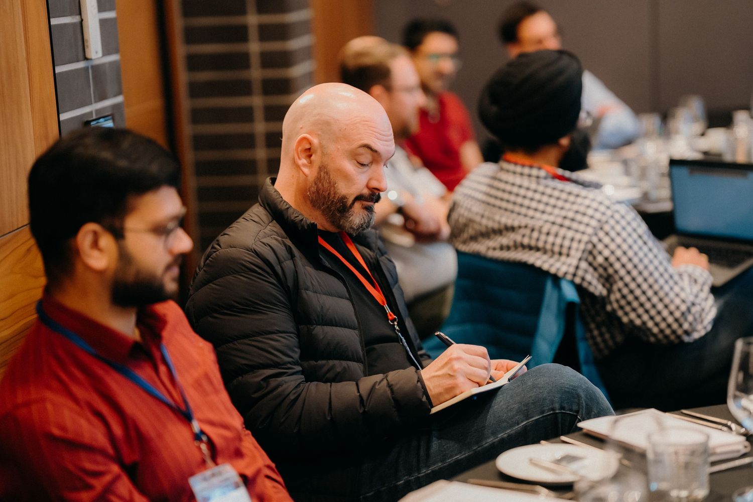 Business professionals sitting at tables during a conference or meeting in an office setting.