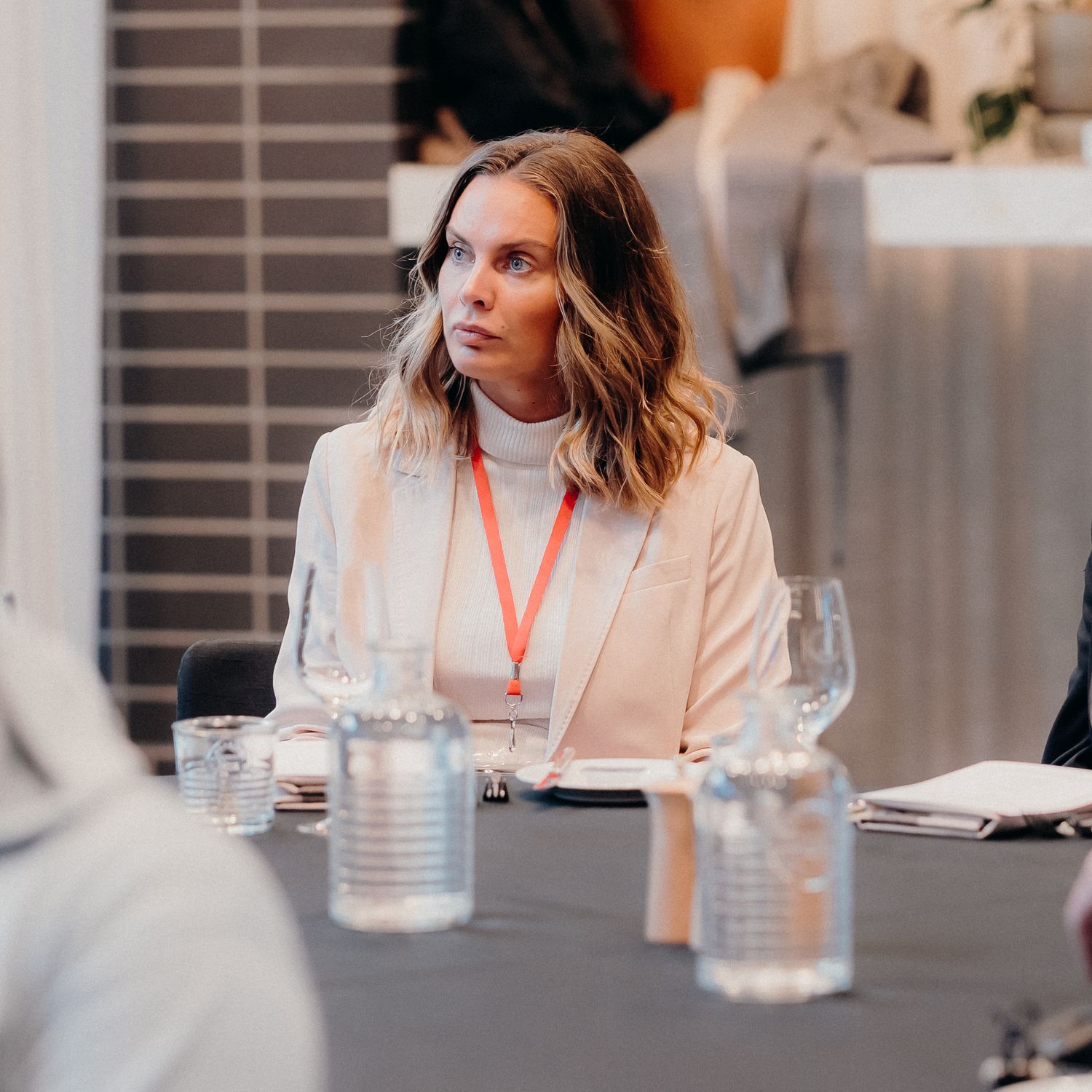 Professional wearing a cream blazer sits attentively at a business conference table during a meeting.