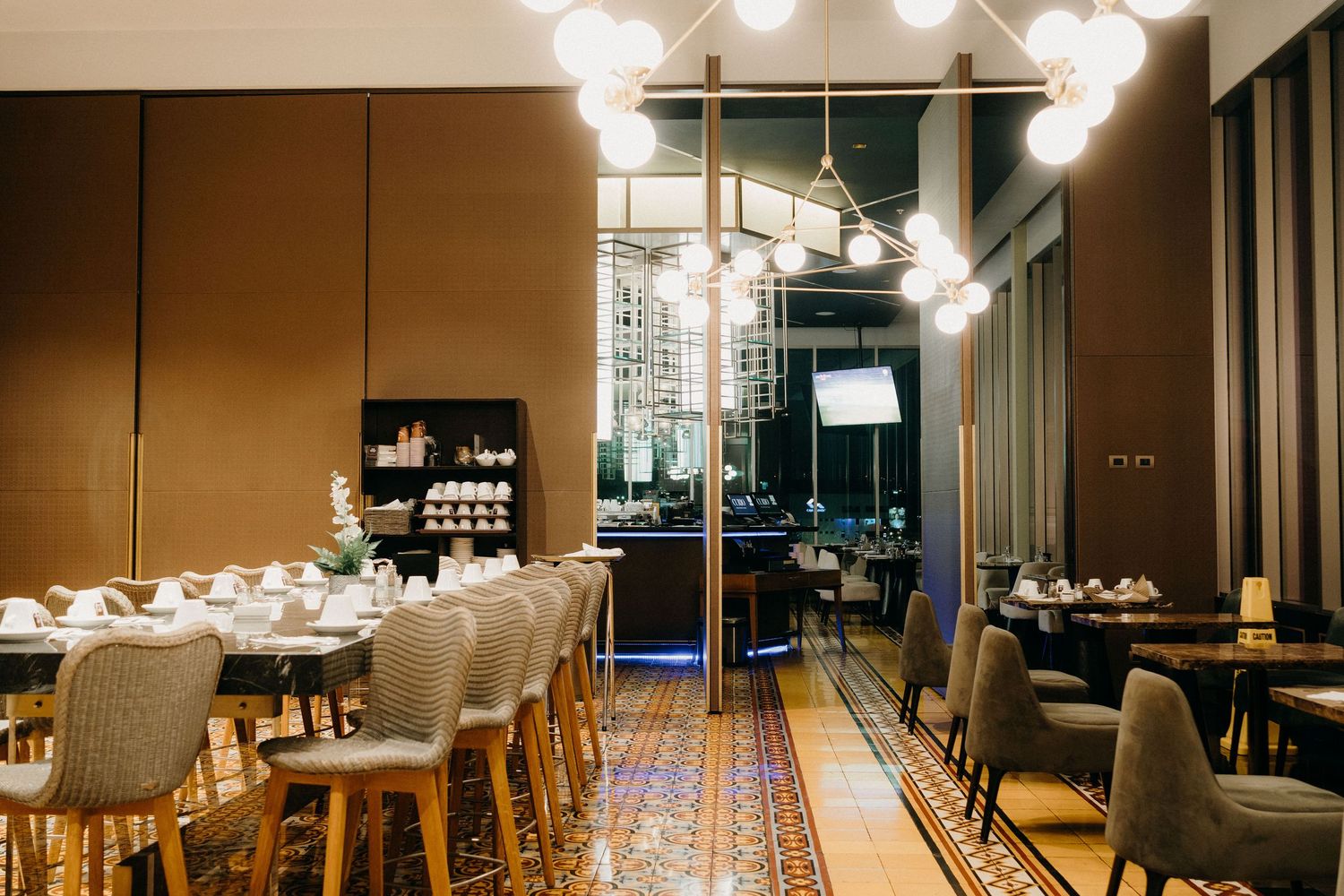Modern restaurant interior with warm lighting, wood paneling, and multiple dining tables arranged in a long hallway.
