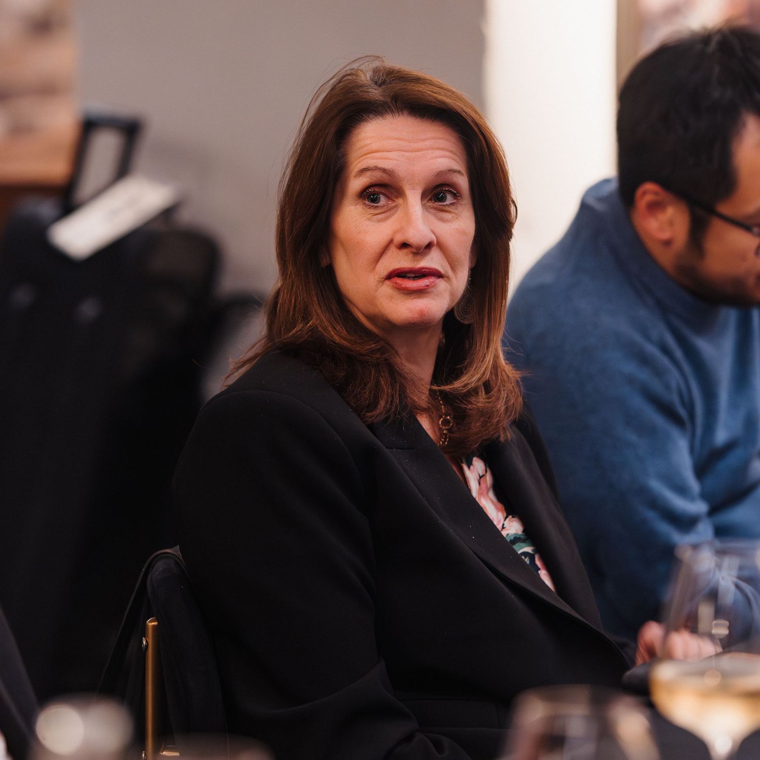 A person in business attire is shown in profile during what appears to be a professional meeting or conference.