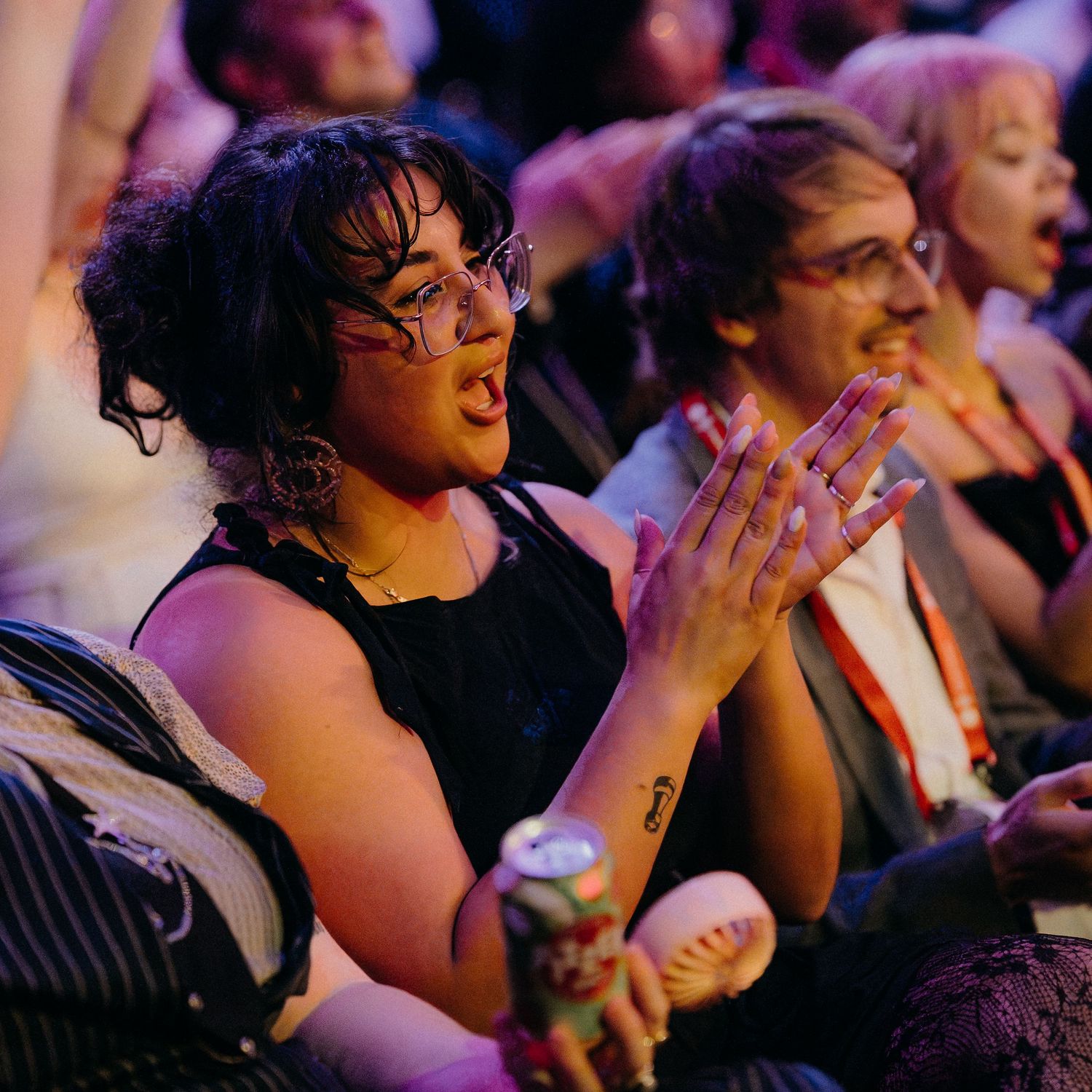 Audience members laugh and react with joy during a live performance in a dimly lit theater.