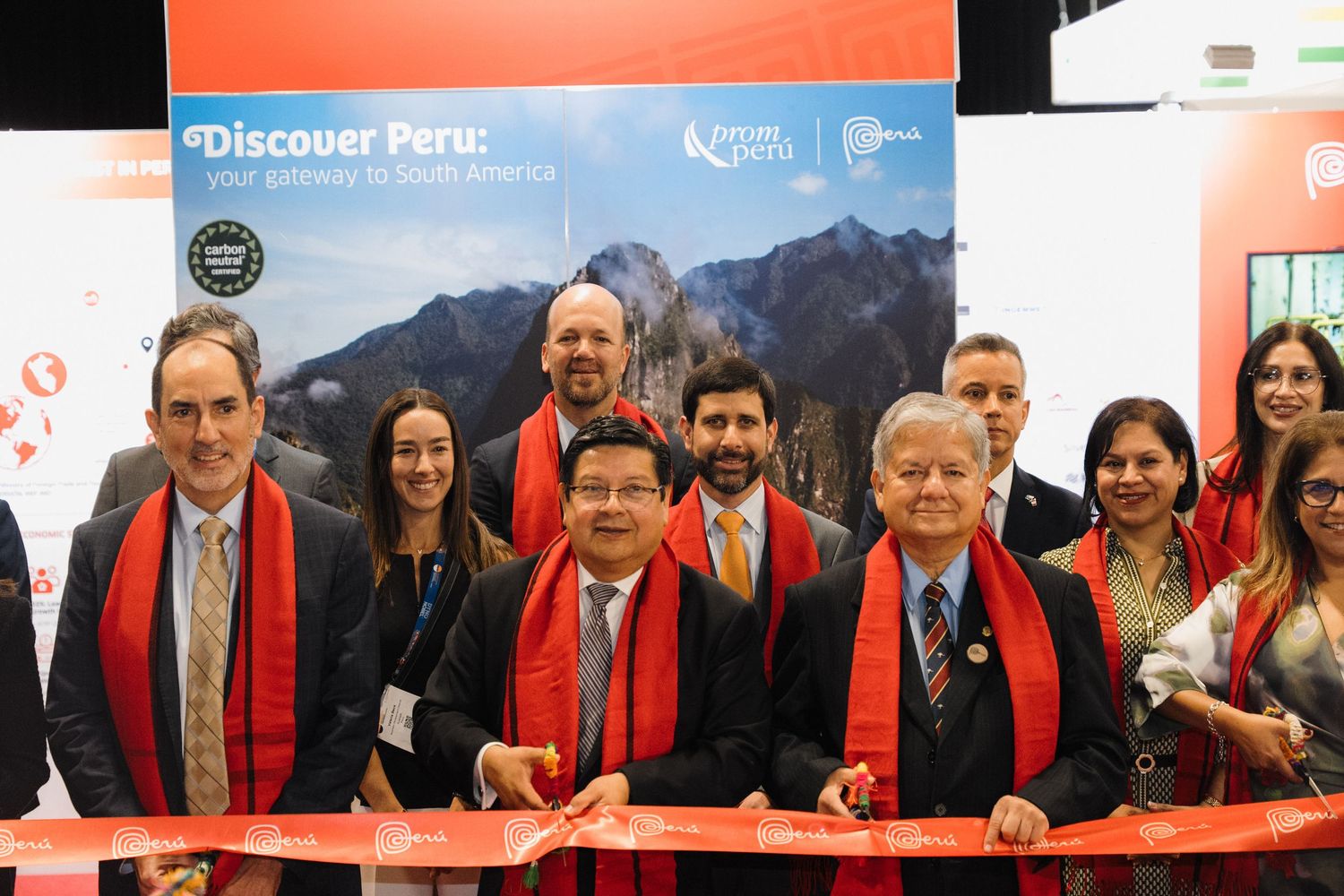 A group wearing red scarves and dark suits stand together at a ceremonial ribbon cutting event.