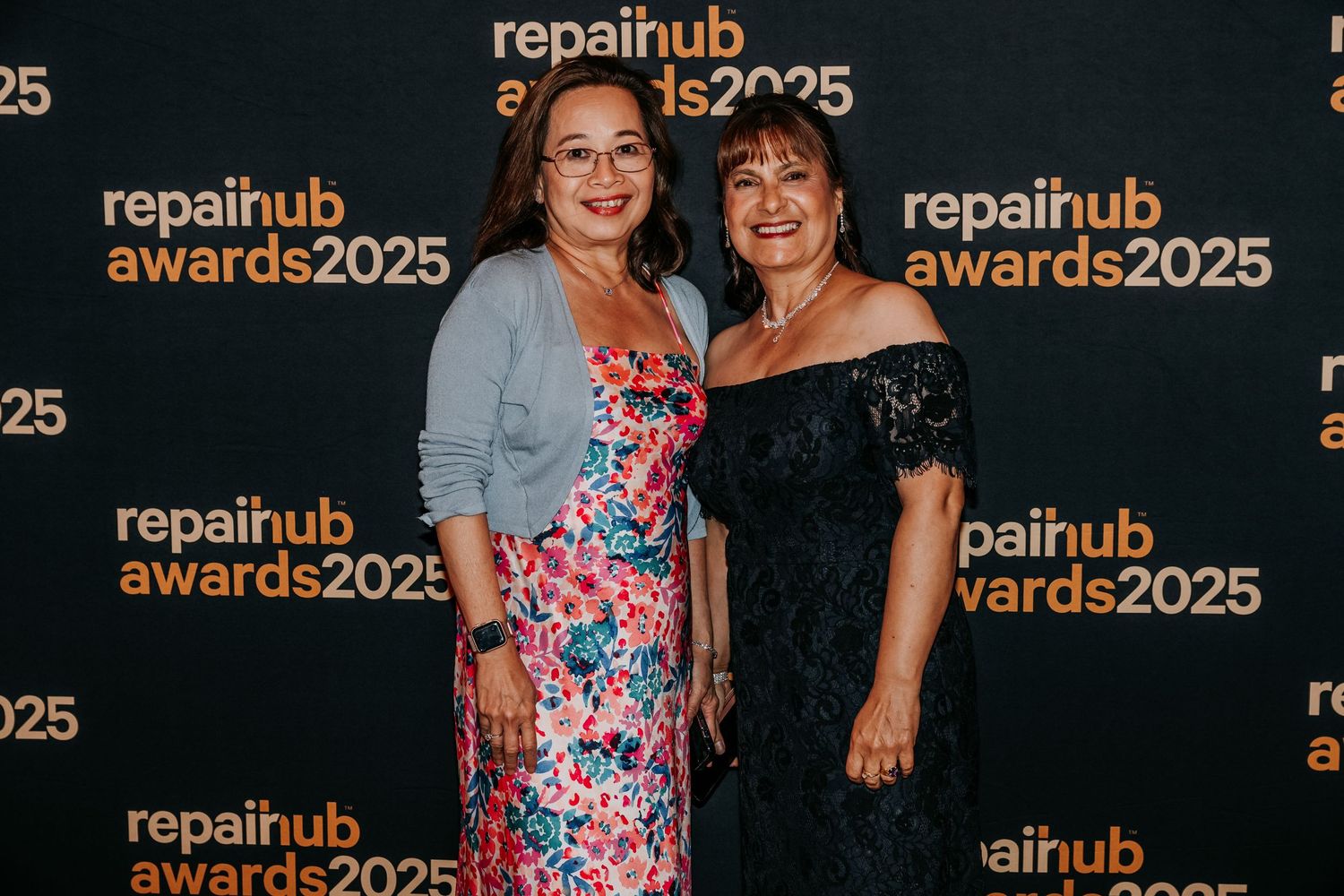 Two attendees pose together at the Repairhub Awards 2025 event in front of branded backdrop.