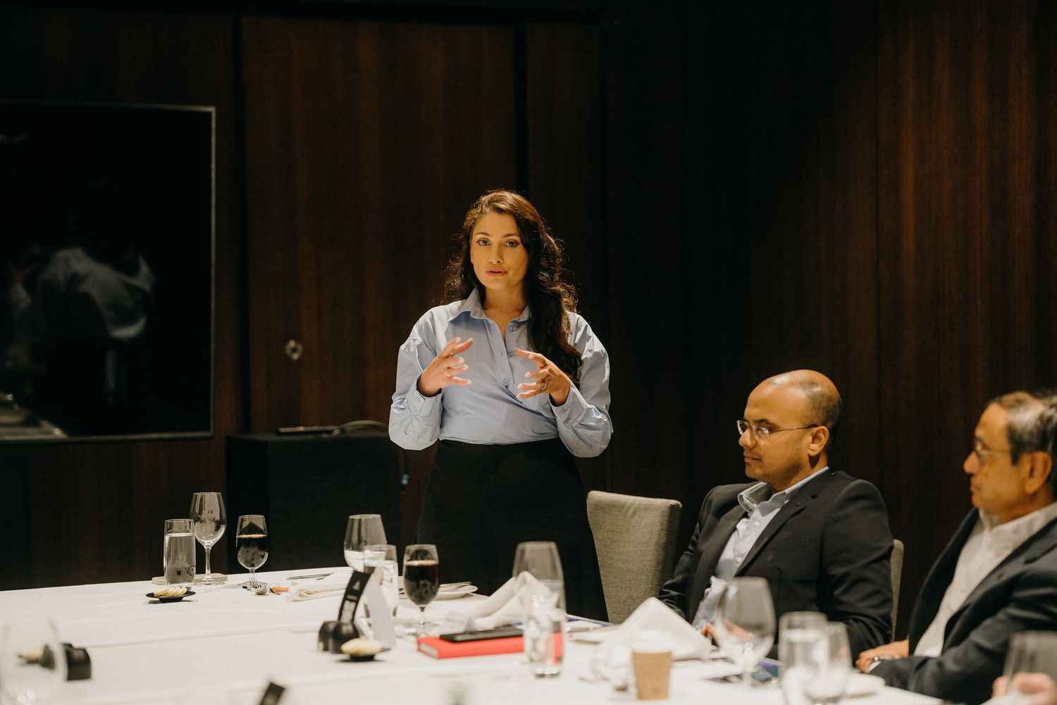 Professional woman presenting at a business dinner meeting with colleagues seated at an elegant table.