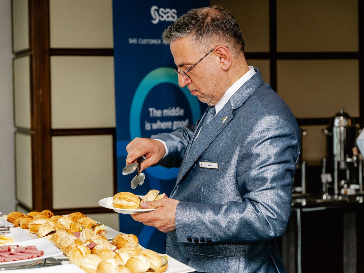 Man in gray suit serving food at a SAS Customer Intelligence conference catering table with rolls and appetizers.