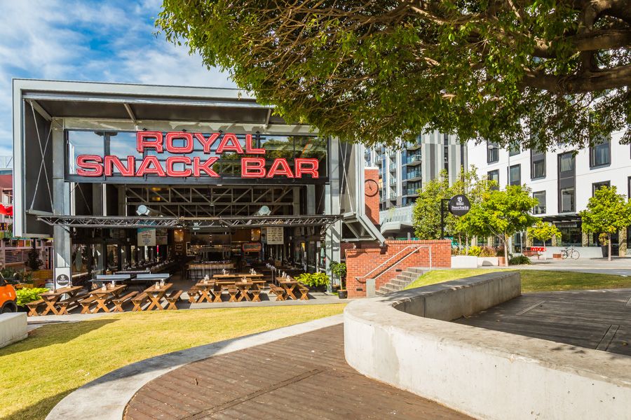 Modern restaurant exterior combines glass walls and wooden accents with outdoor seating under blue skies.