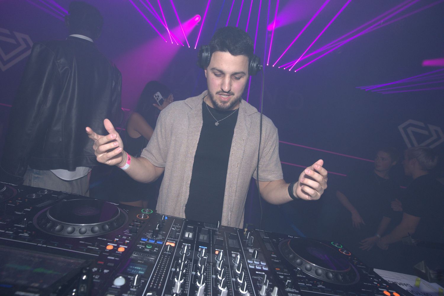 DJ performs behind glowing mixing deck with purple lights illuminating nightclub atmosphere.