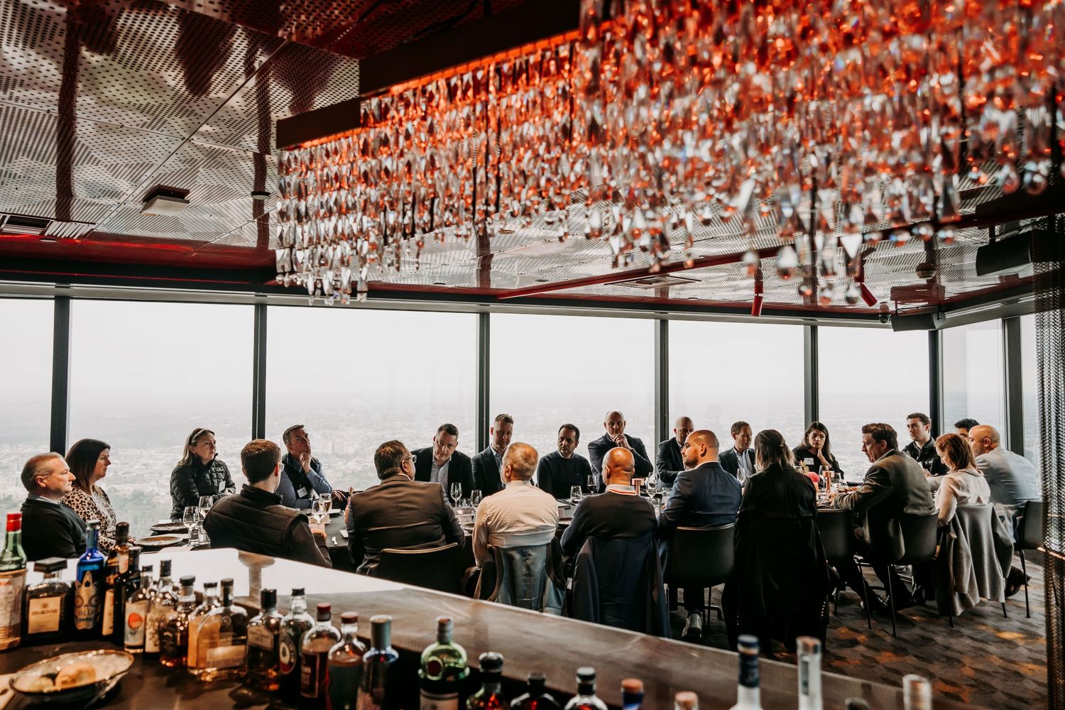 Restaurant patrons dine at communal tables under hanging red lanterns in a modern space with floor-to-ceiling windows.