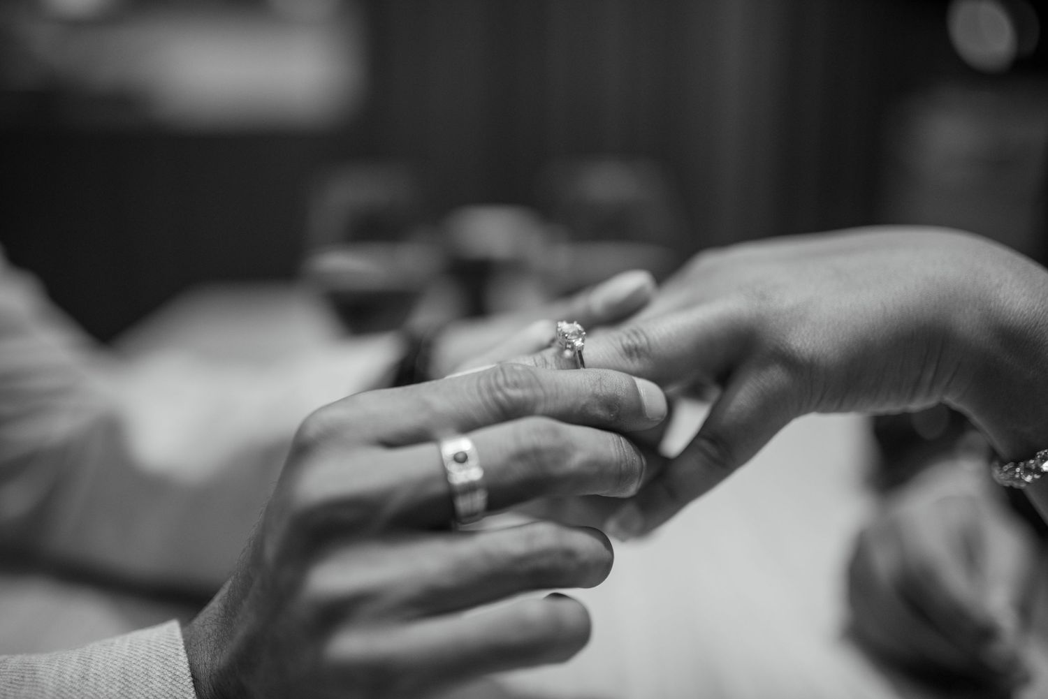 A black and white image showing hands placing a wedding ring onto a finger during a marriage ceremony.
