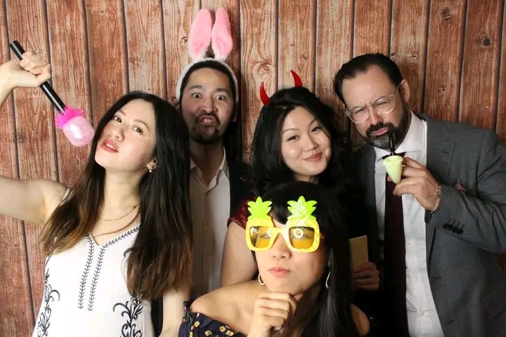 A series of photo booth style snapshots showing people posing and having fun against a wooden wall background.