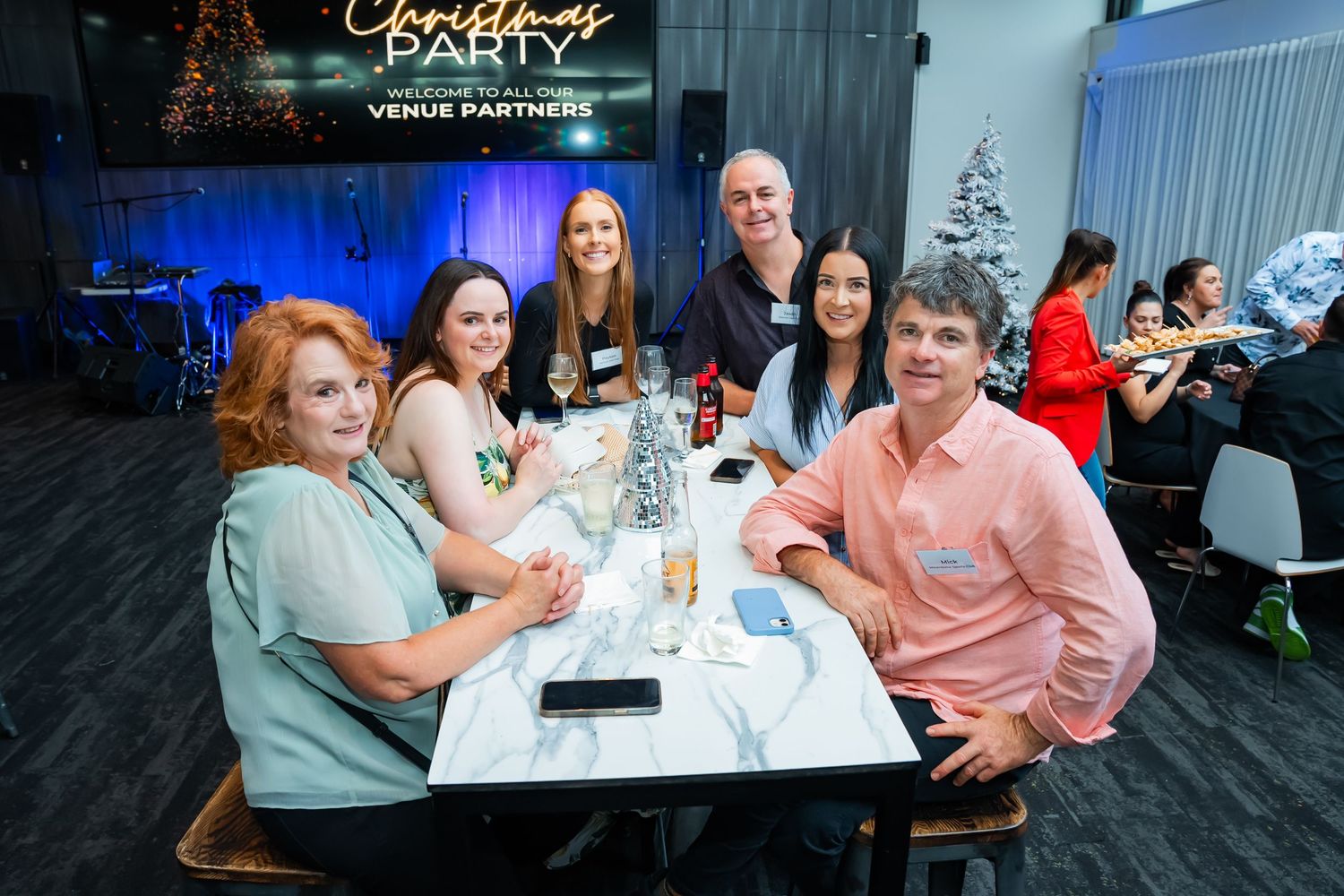 People seated at tables during a business conference or networking event in a modern venue with blue lighting.