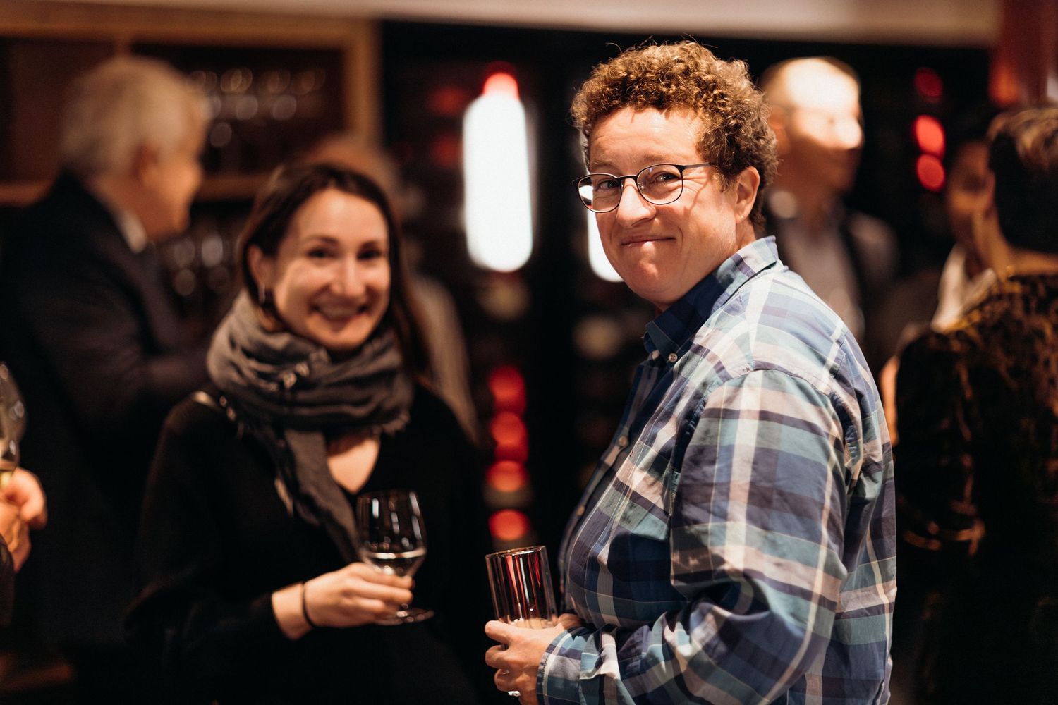 People enjoying drinks and conversation at a dimly lit social gathering or networking event.