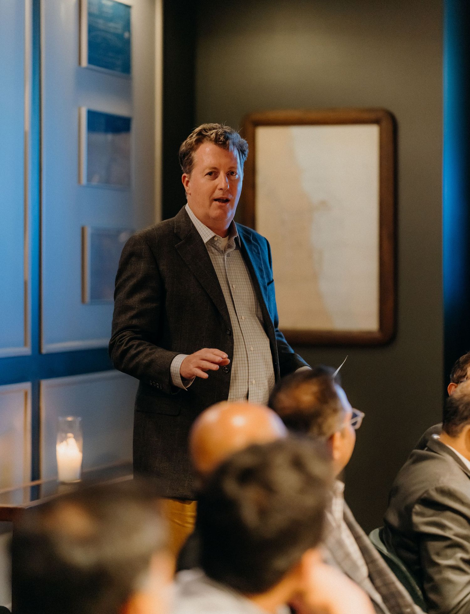 Business professionals gathered in a meeting room with blue-paneled walls and candlelit tables for a corporate event.
