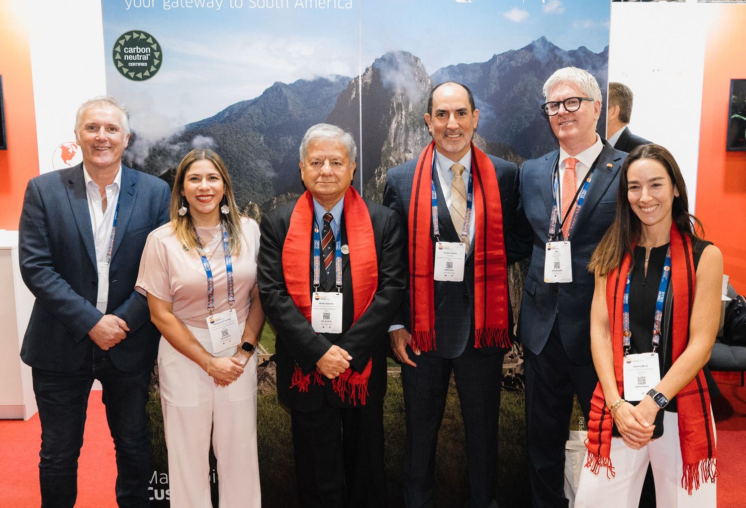A group of six people wearing conference badges pose together at an event with mountain backdrop.