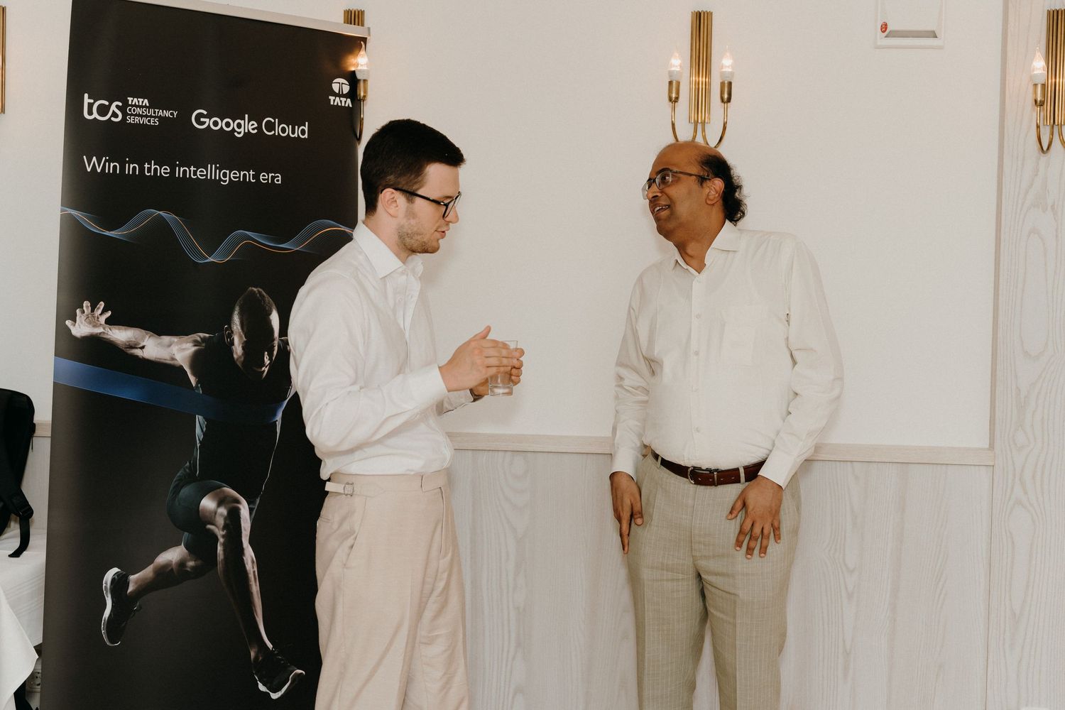 Two professionals networking at a TCS and Google Cloud event, discussing business in an elegant venue.