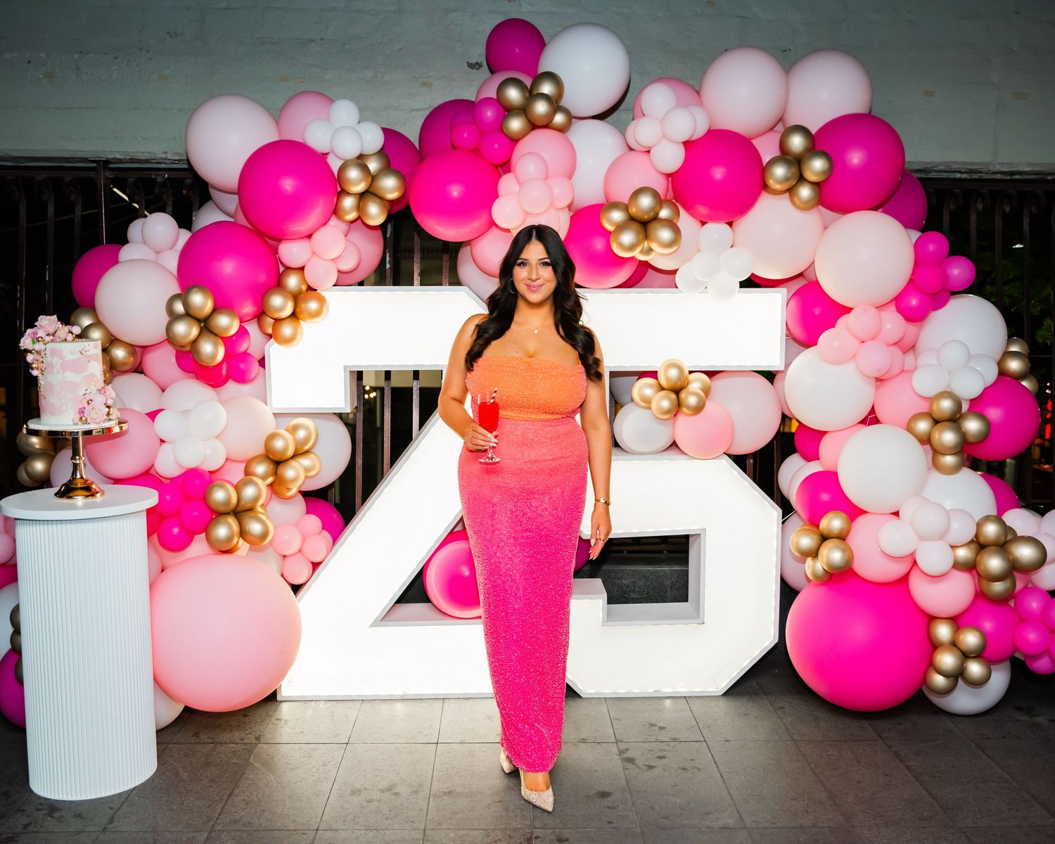 Elegant balloon garland installation in pink, white and gold creates a festive arch decoration against a dark wall.