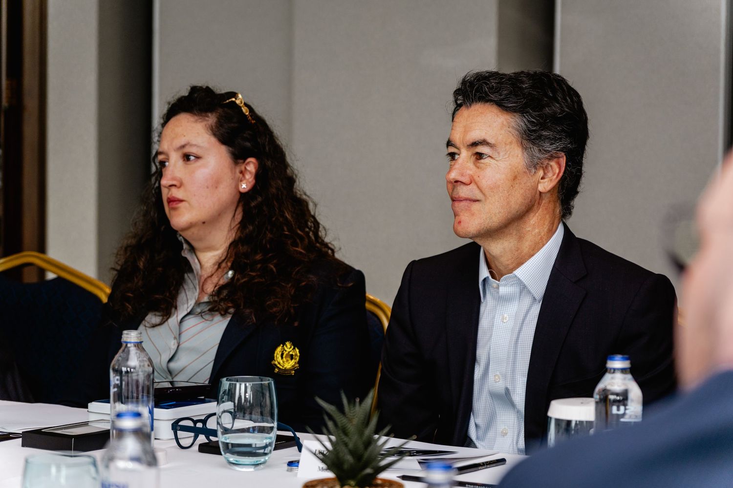 Two professionals seated at a conference table during a business meeting, listening attentively to a presentation.