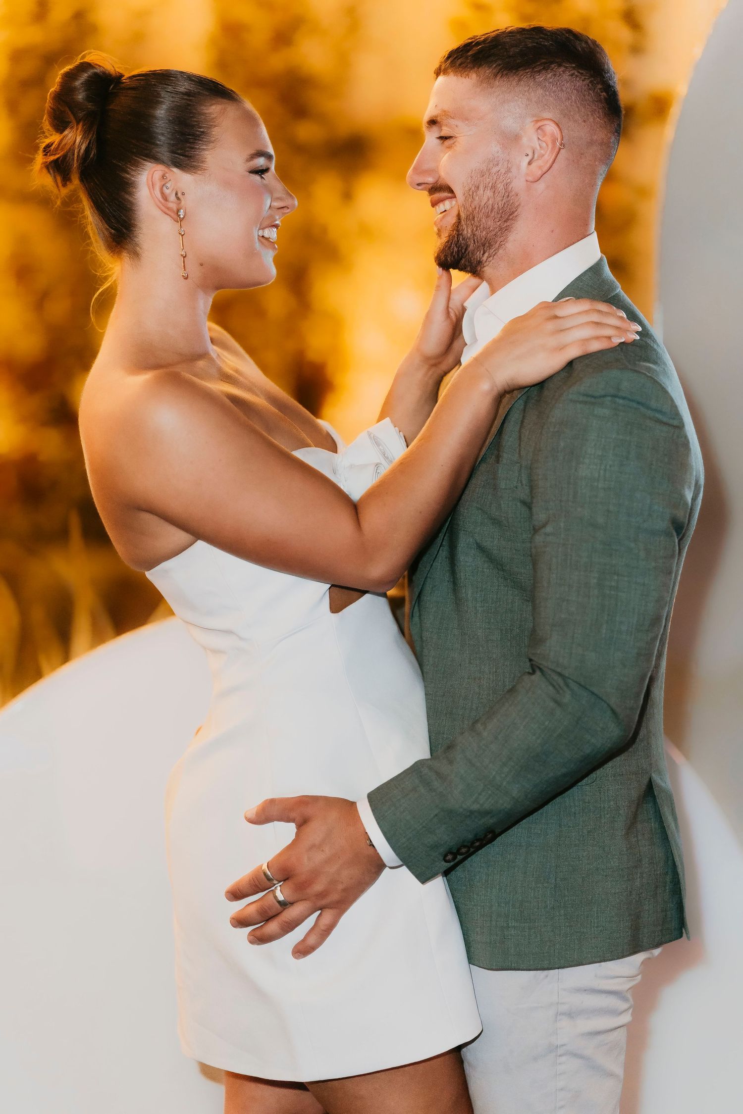 Romantic couple embraces during a photoshoot with warm golden sunset lighting in the background.