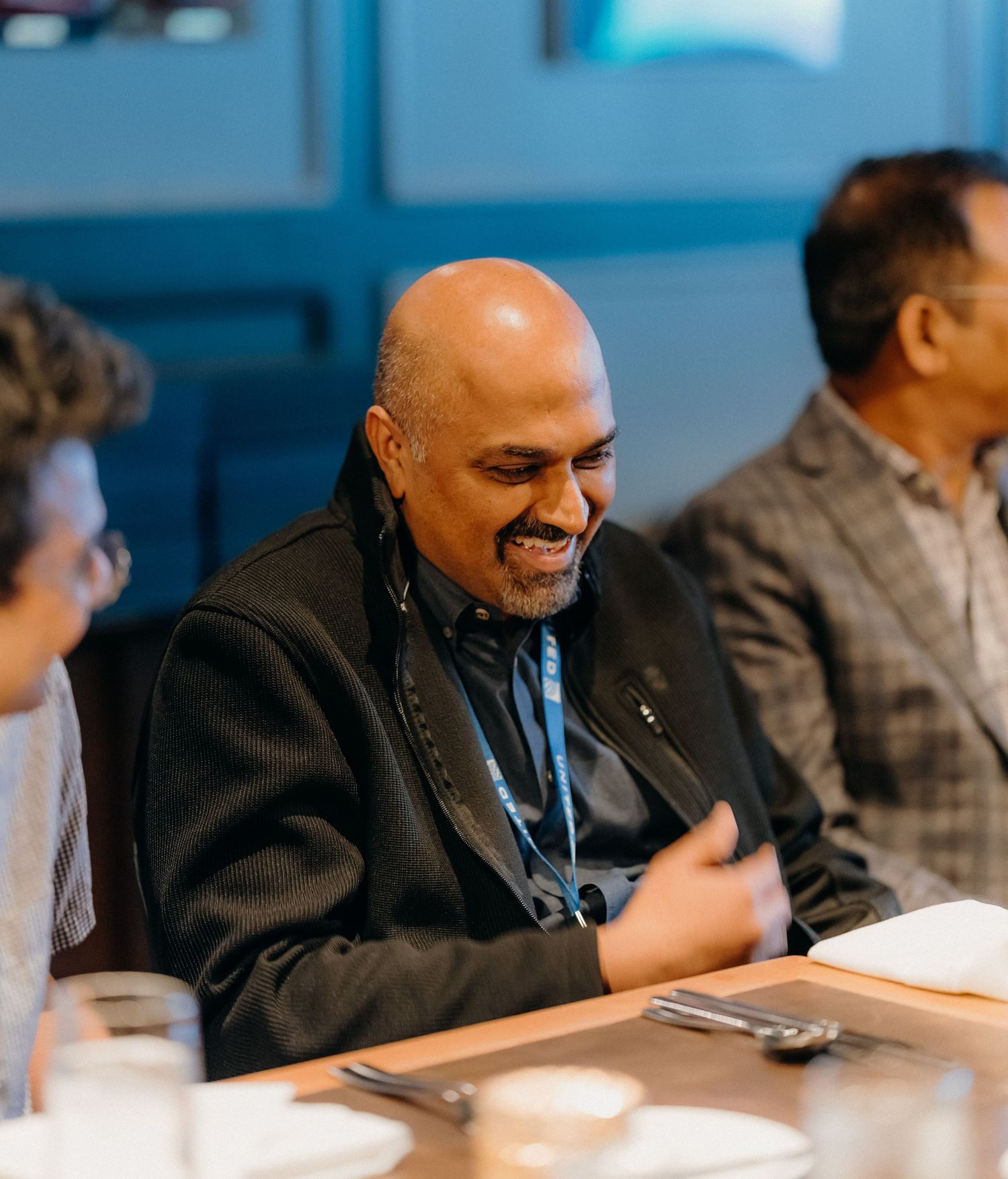 A person in a dark suit sits at a table during a business meeting or conference.