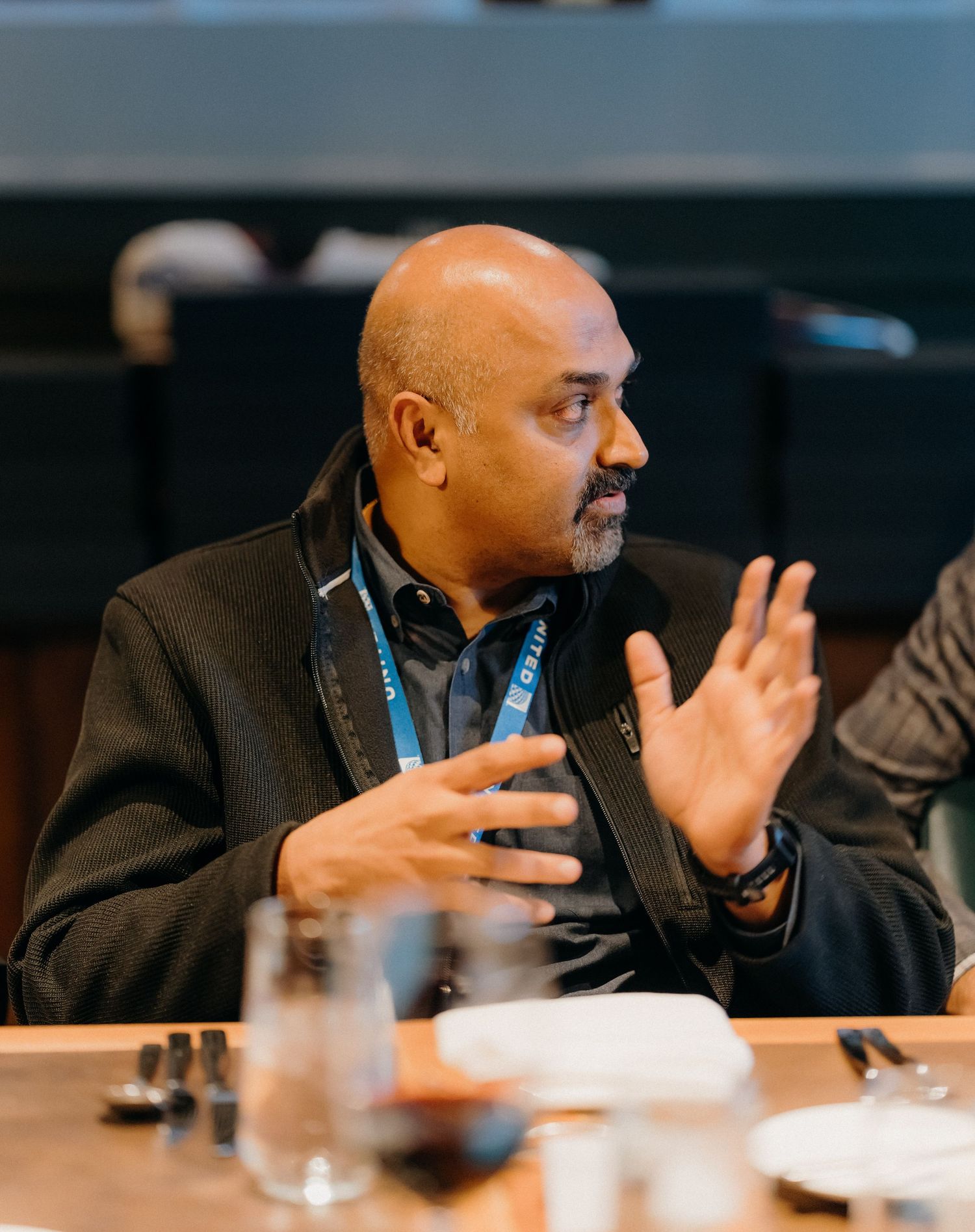Speaker gesturing with hands during a presentation at a conference table.