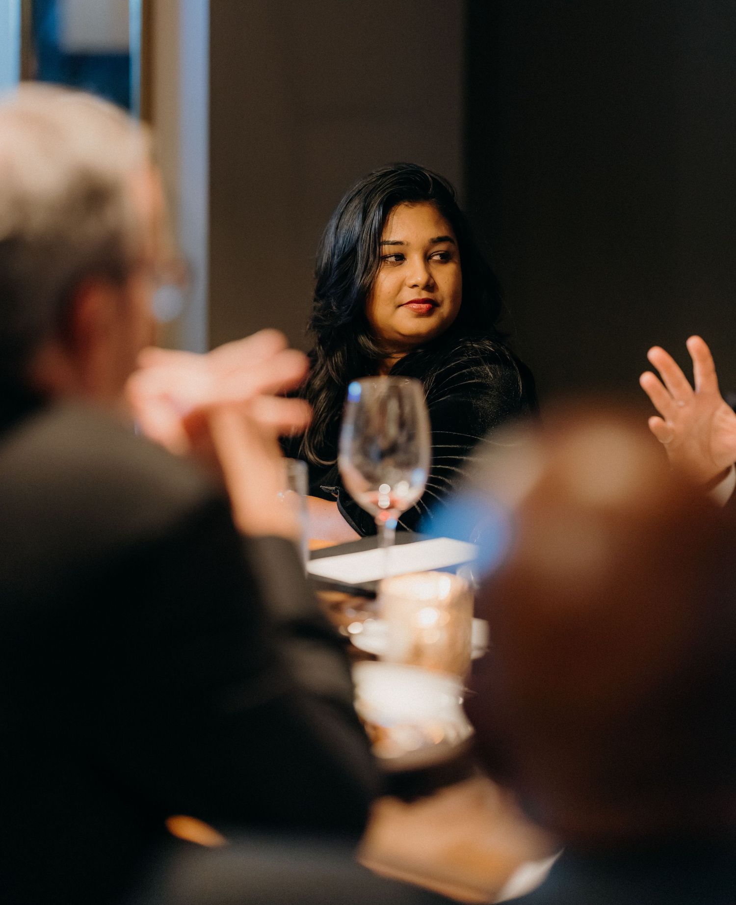 People engaged in focused discussion during a business meeting in a dimly lit conference room.