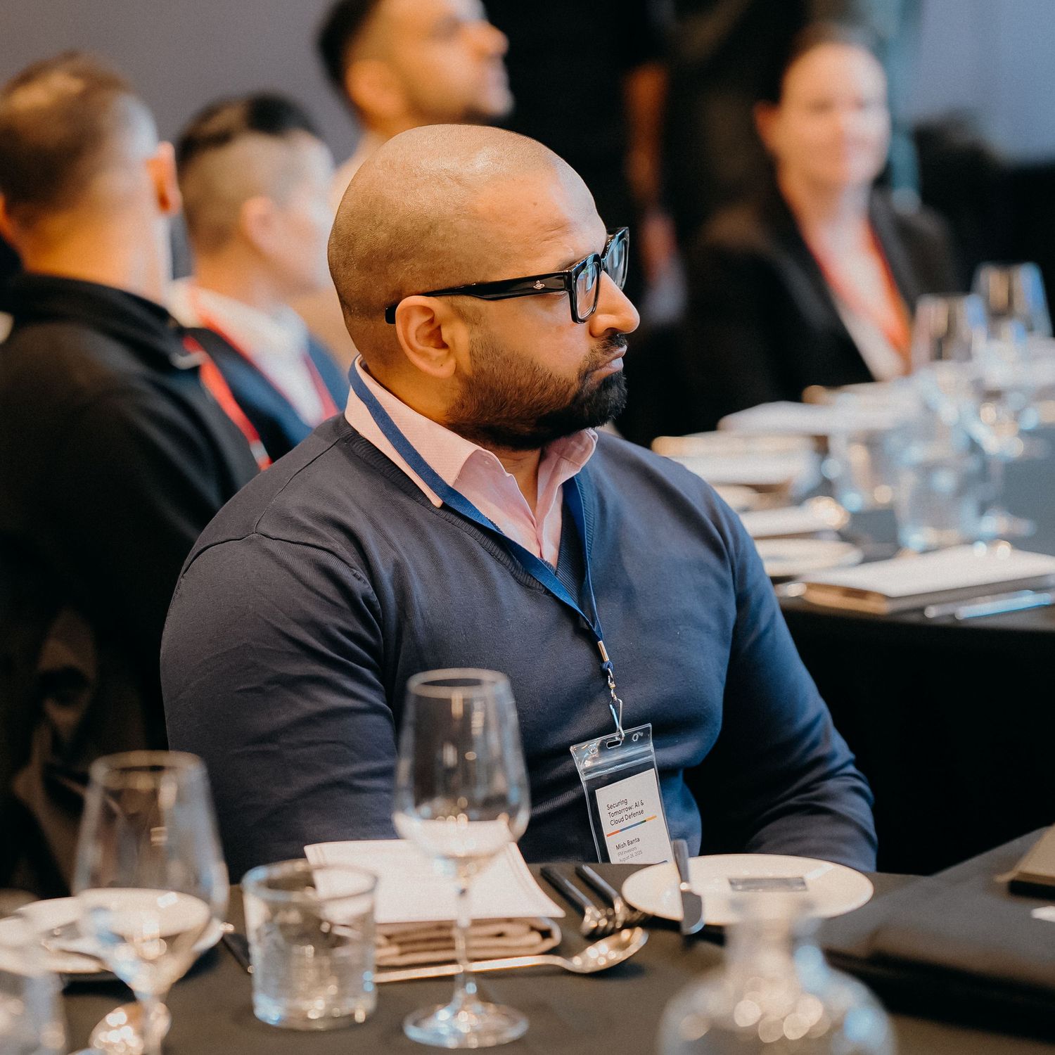 Professional attendee in glasses and pink shirt listening intently during business conference at dining table.