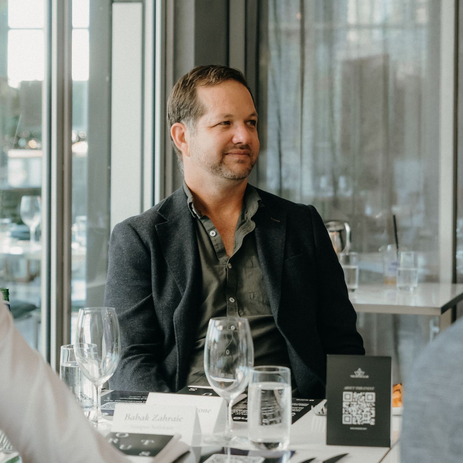Business professionals in dark suits gather around a dining table in an upscale restaurant setting.