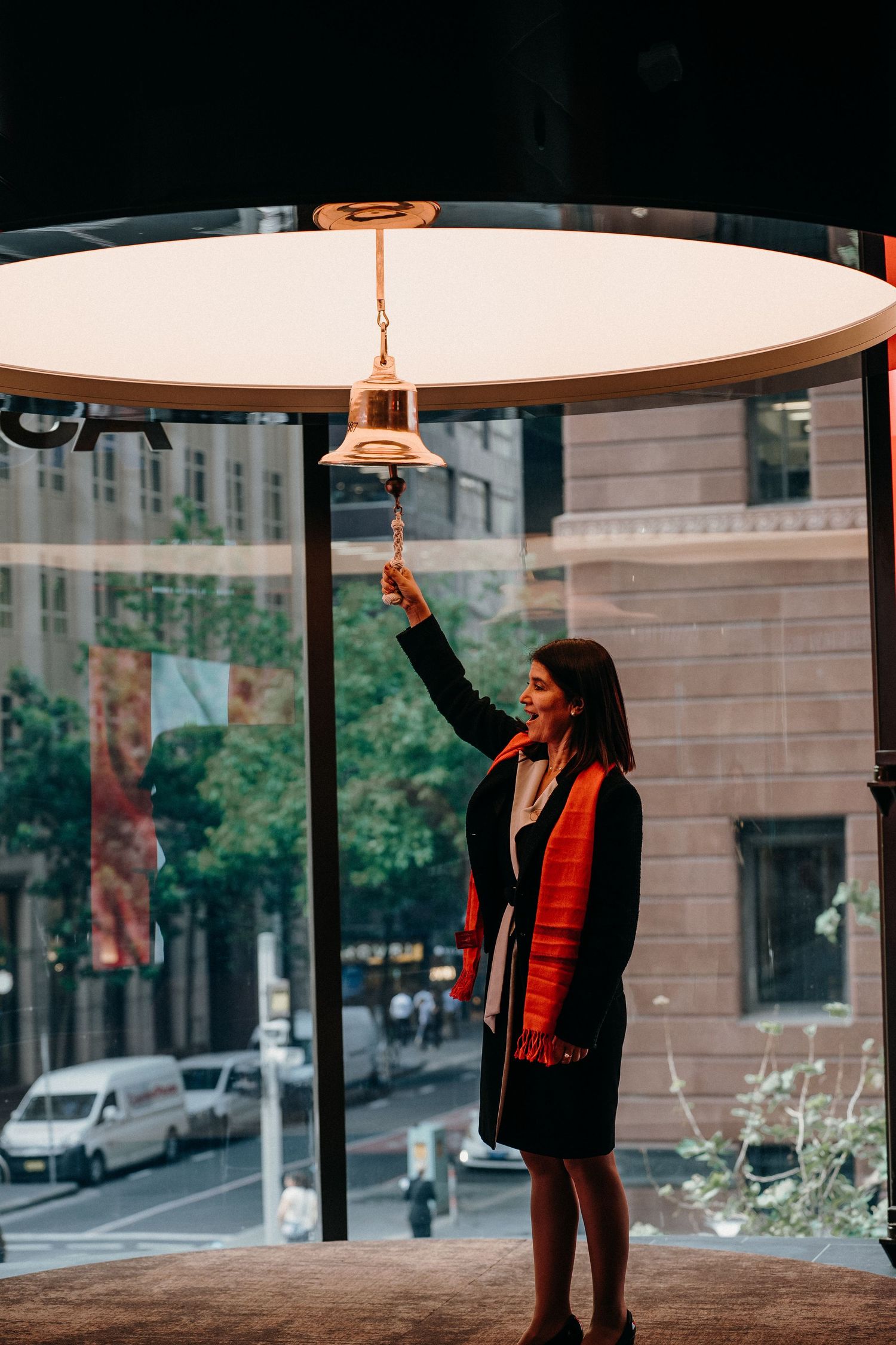 A person in a black jacket and red scarf dances under a circular ceiling light in an urban setting.