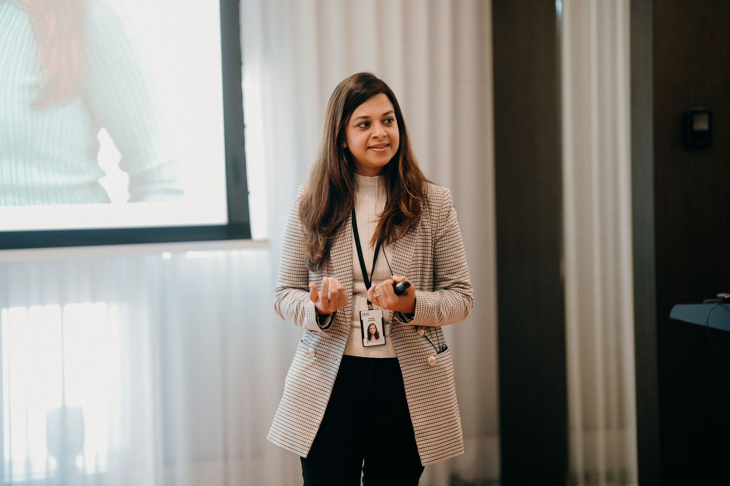 A professional speaker gives a presentation in a conference room wearing a beige blazer.