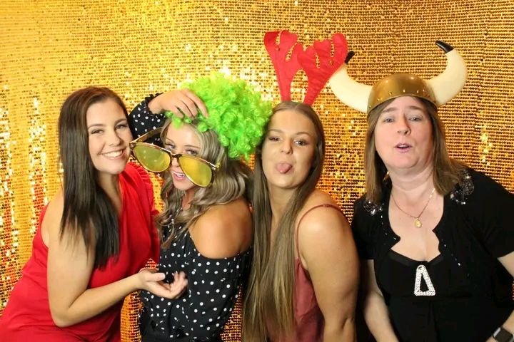 Group of people posing playfully against a golden backdrop with colorful party props and festive decorations.