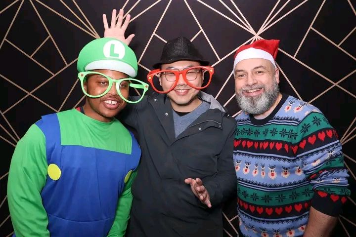 A group of people at a party wearing festive holiday sweaters and colorful costumes pose together for photos.