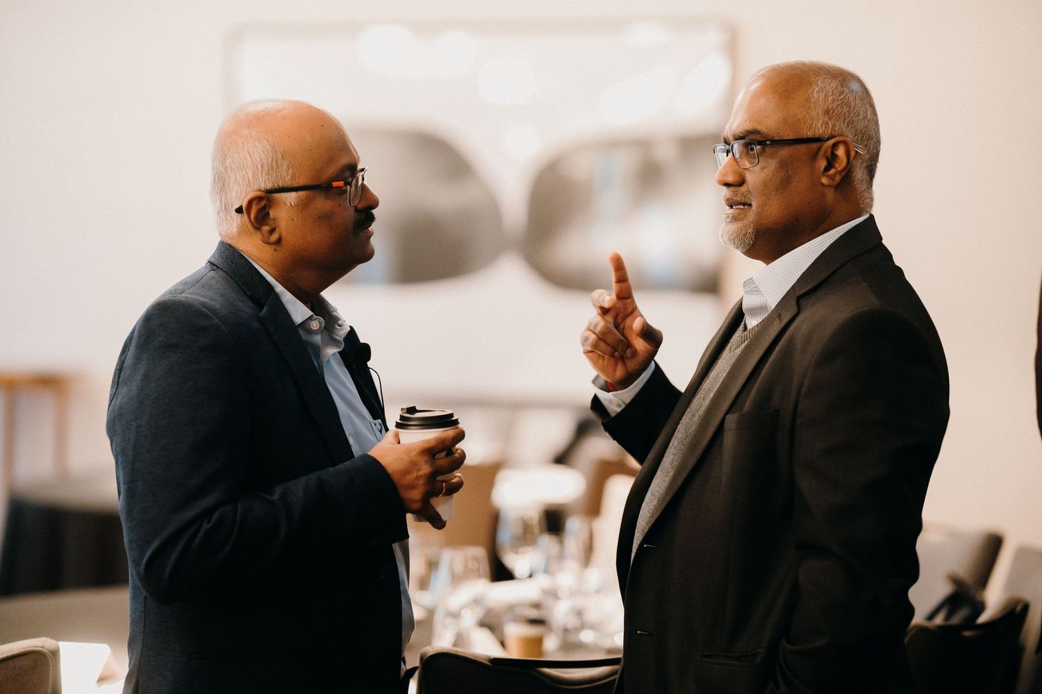 Two business professionals in suits engaged in animated conversation at a networking event.
