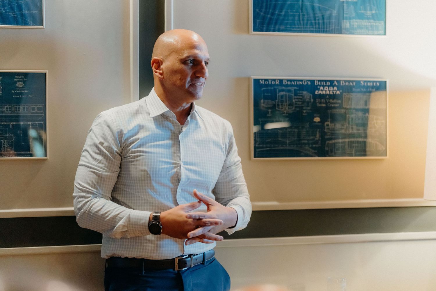 Professional in a white dress shirt leans against office wall while looking at blueprints and documents.