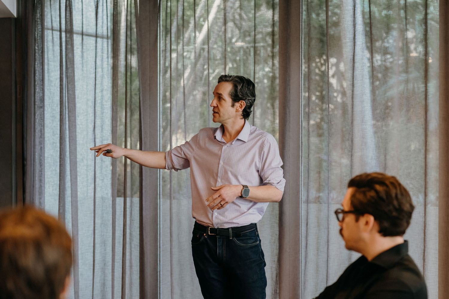 Business professional in pink shirt gestures while giving a presentation in modern office meeting room.