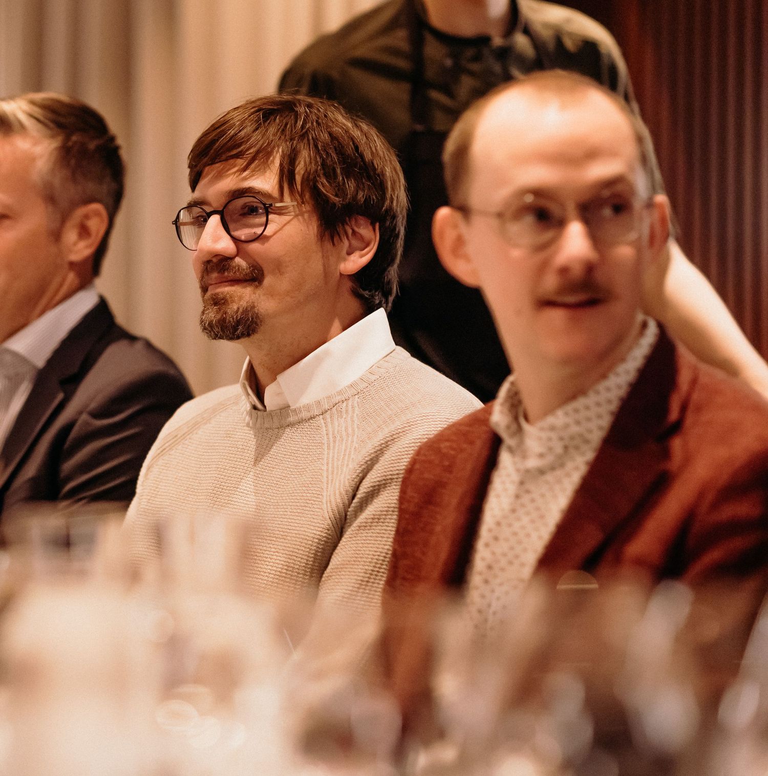 A group of people with mustaches sit together in formal attire at what appears to be a social gathering.