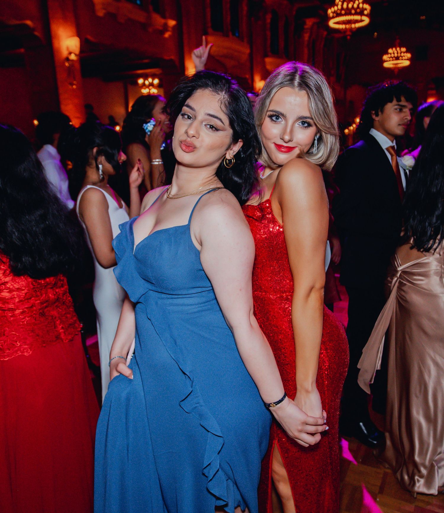 Two friends share a happy moment on the dance floor at an atmospheric event with red lighting.