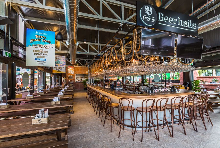Modern restaurant interior with wooden tables and chairs featuring geometric ceiling lights and exposed industrial elements.