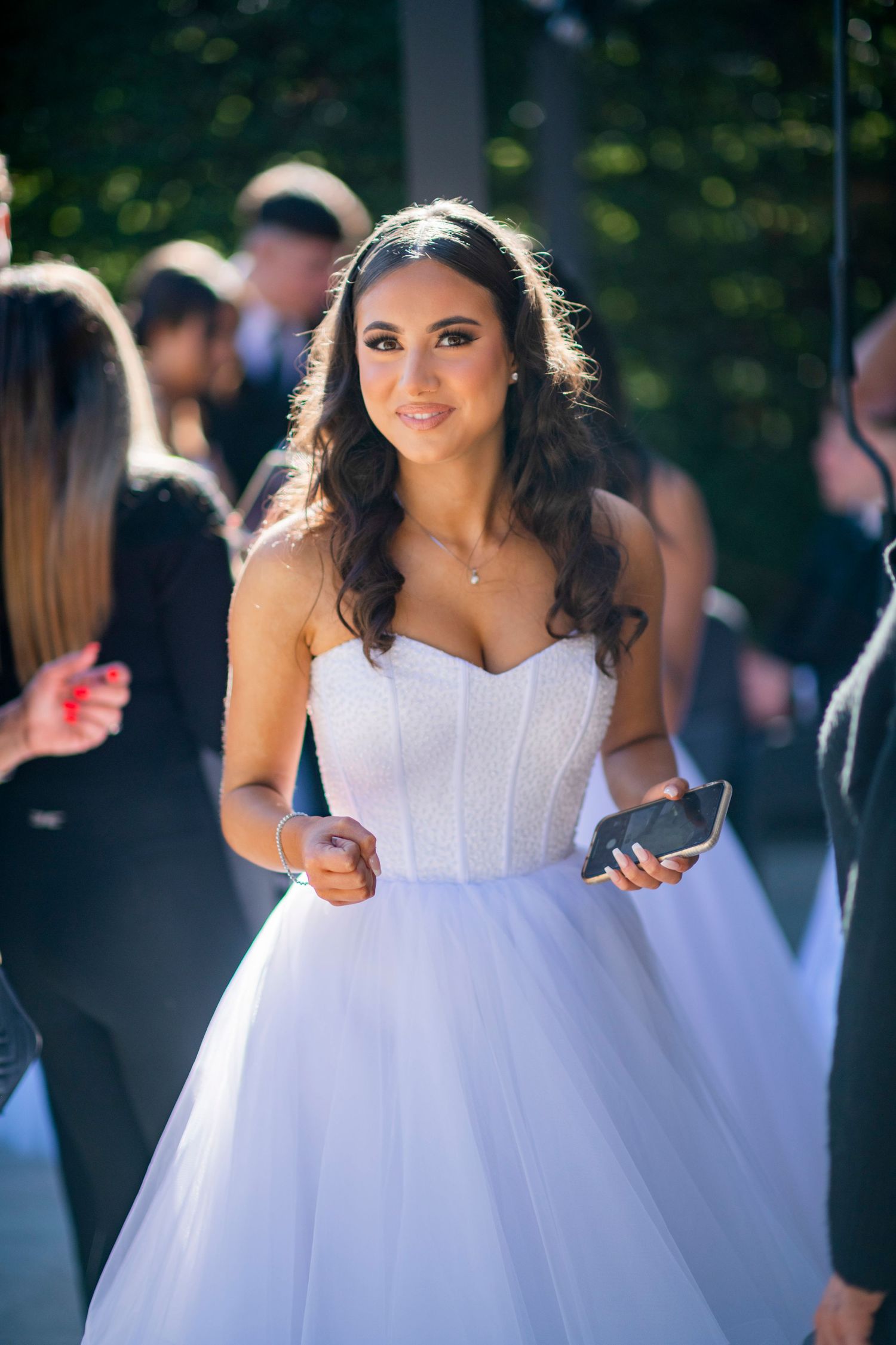 A bride in a white strapless ballgown with tulle skirt checks her phone while walking outdoors.