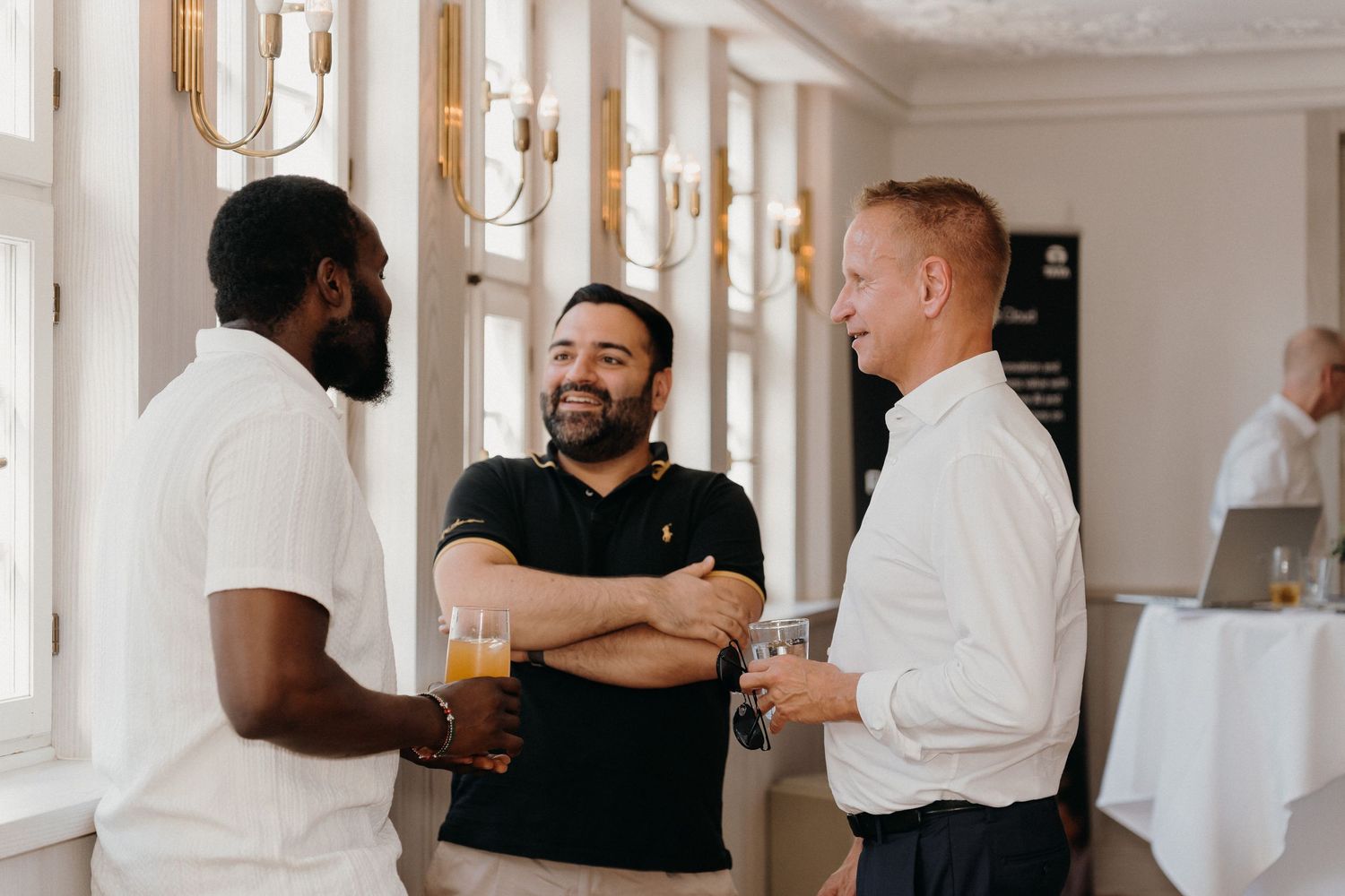 Three men socializing at an elegant indoor event, one holding a beer glass, smiling and engaged in conversation.