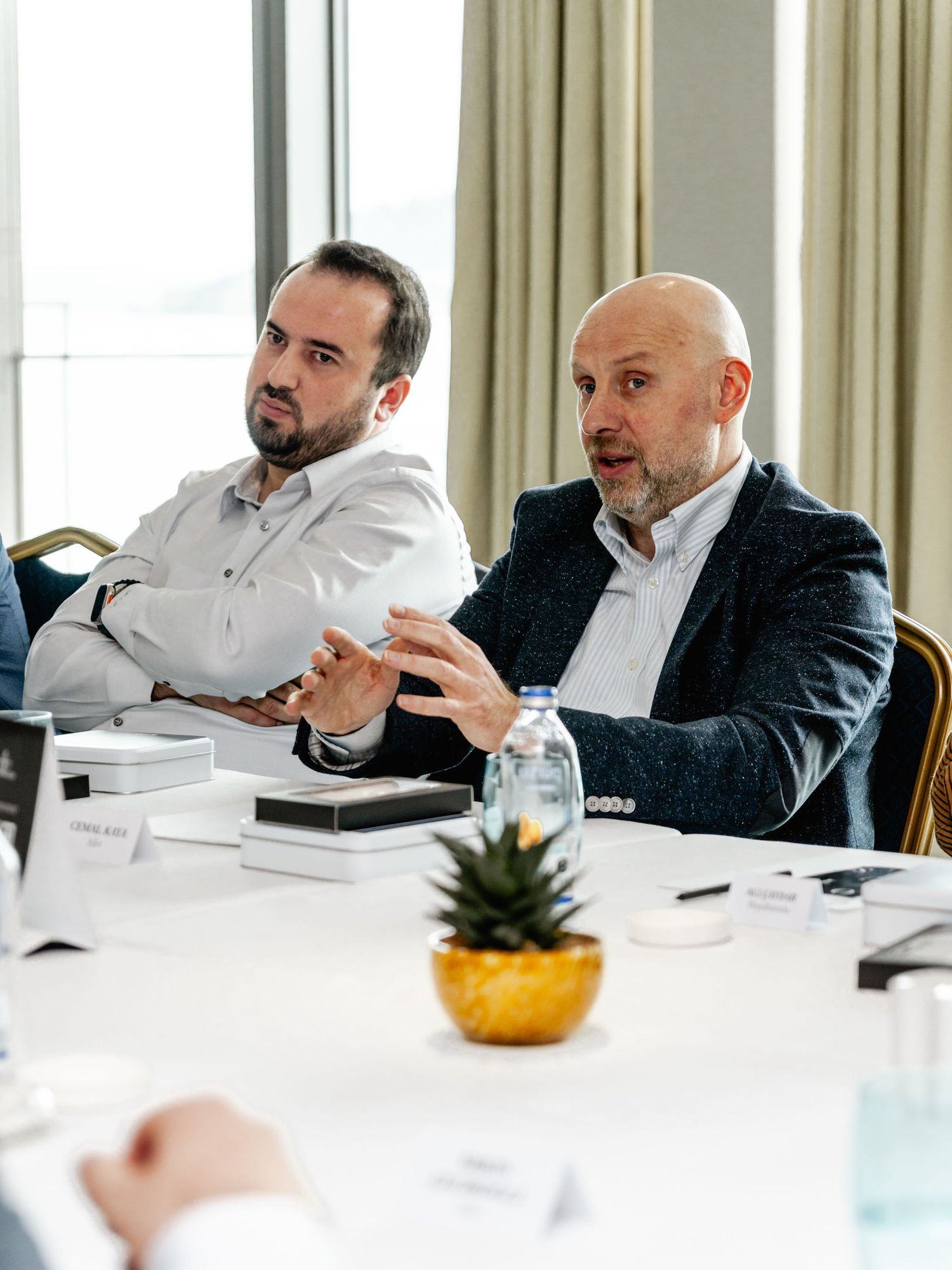 Two businessmen in suits sit at a conference table, engaged in discussion during a professional meeting.