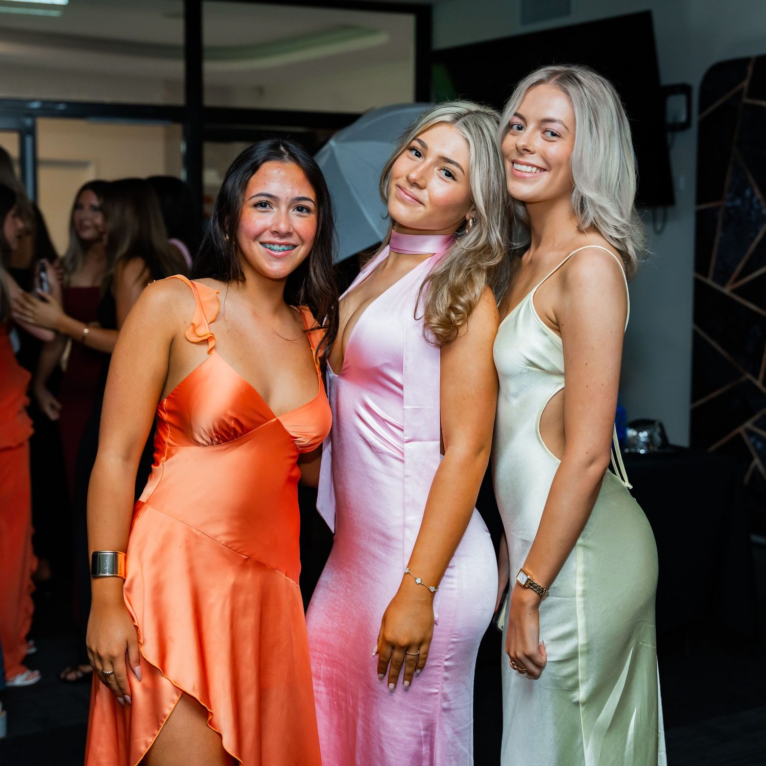 Group of friends in colorful satin bridesmaid dresses posing and laughing together at a wedding celebration.