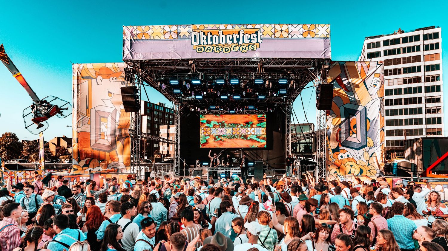 A large crowd gathers at an outdoor music festival with colorful lighting and entertainment.
