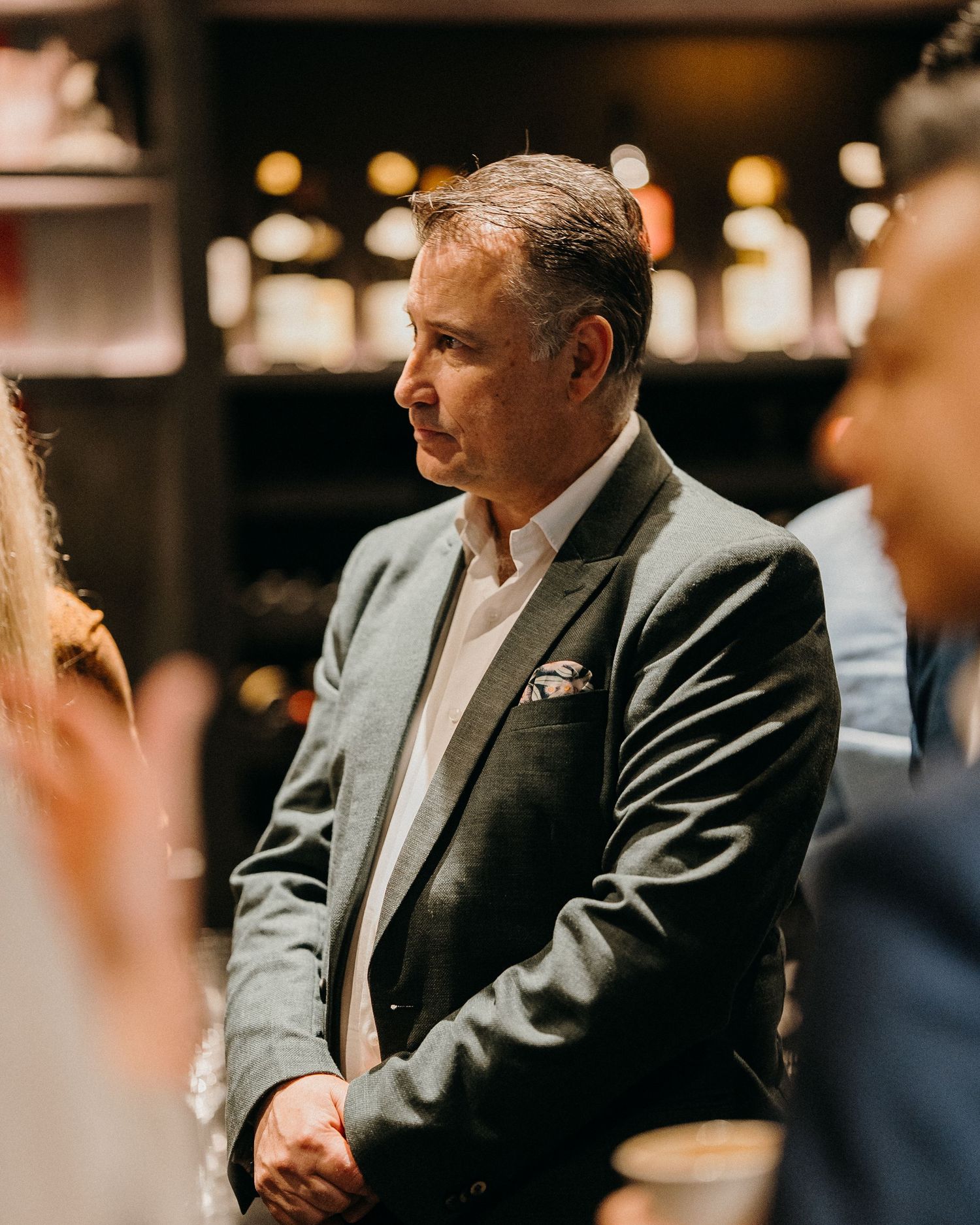 Man in a dark suit jacket sits in conversation during a business meeting in a dimly lit setting.