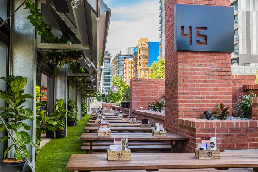 Modern apartment building balcony with wooden seating and planters overlooking the city skyline on a sunny day.