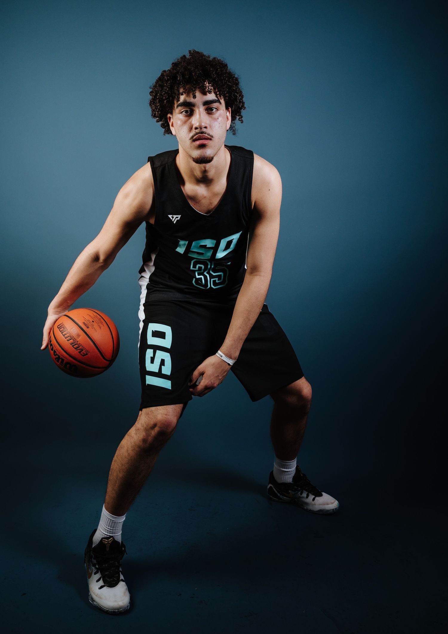 Basketball player in black uniform crouches low while dribbling on dark studio background.