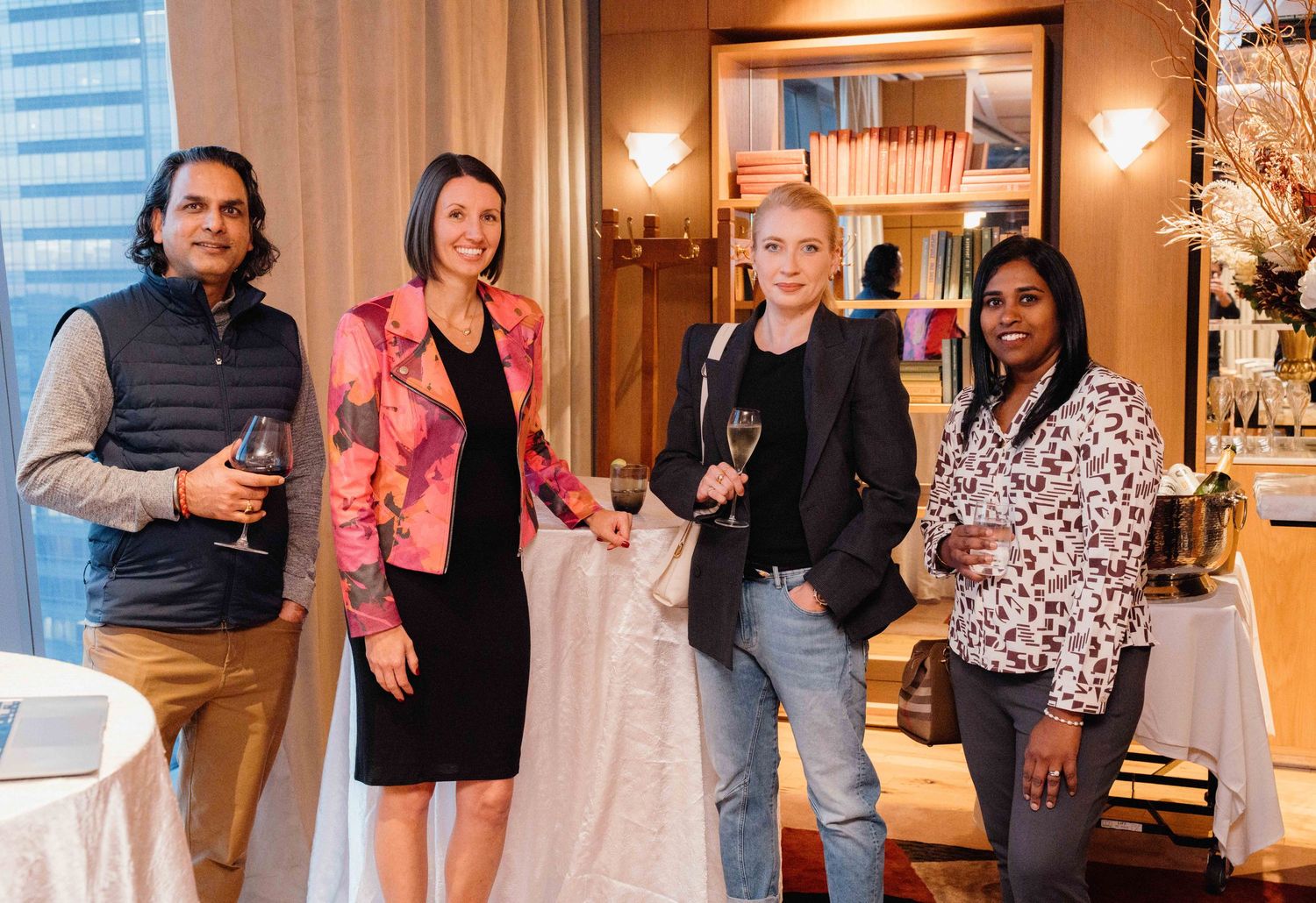 Four people stand together in an elegant room holding wine glasses and smiling at a social gathering.