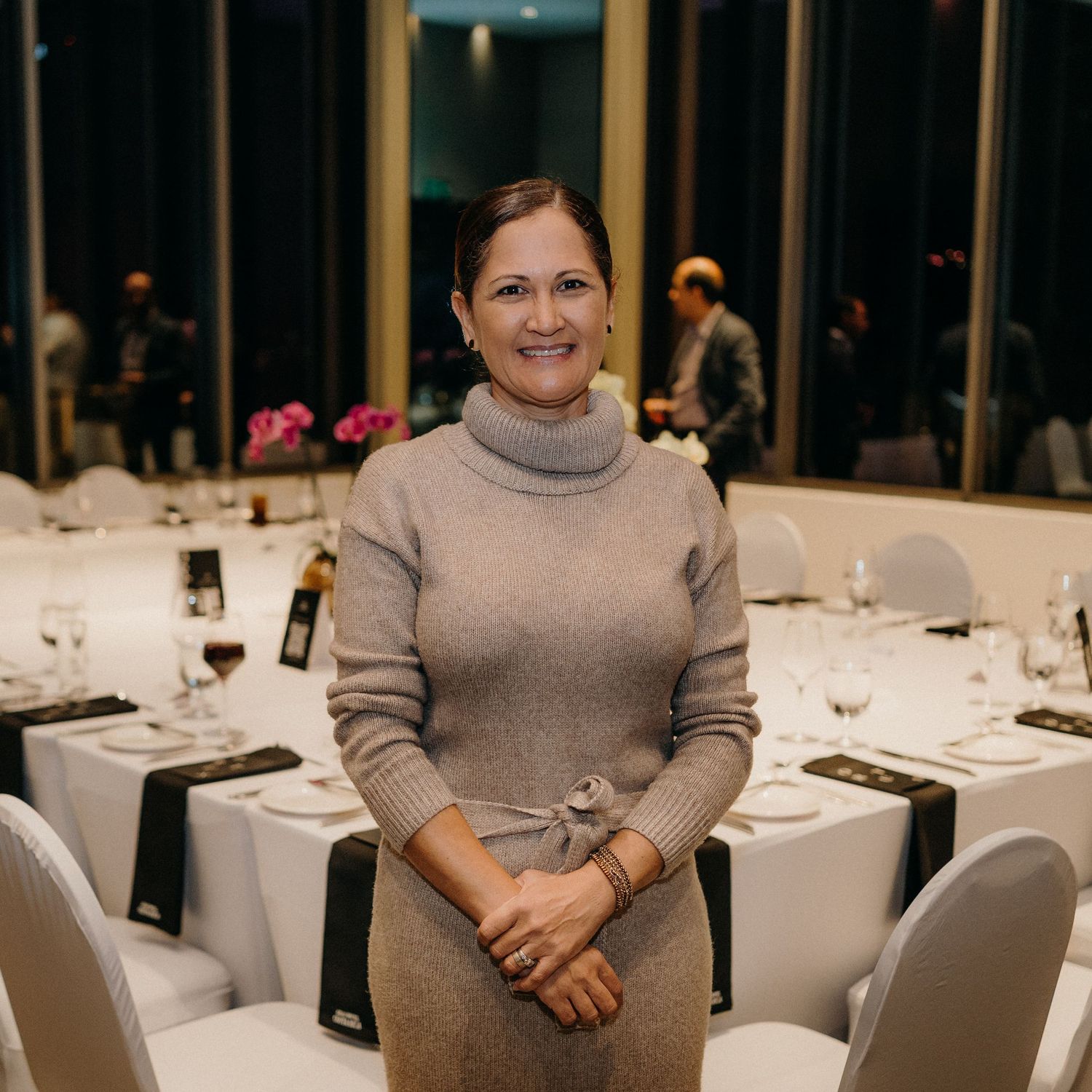 Person wearing a gray turtleneck sweater sits at an elegant table setting in a formal dining room.