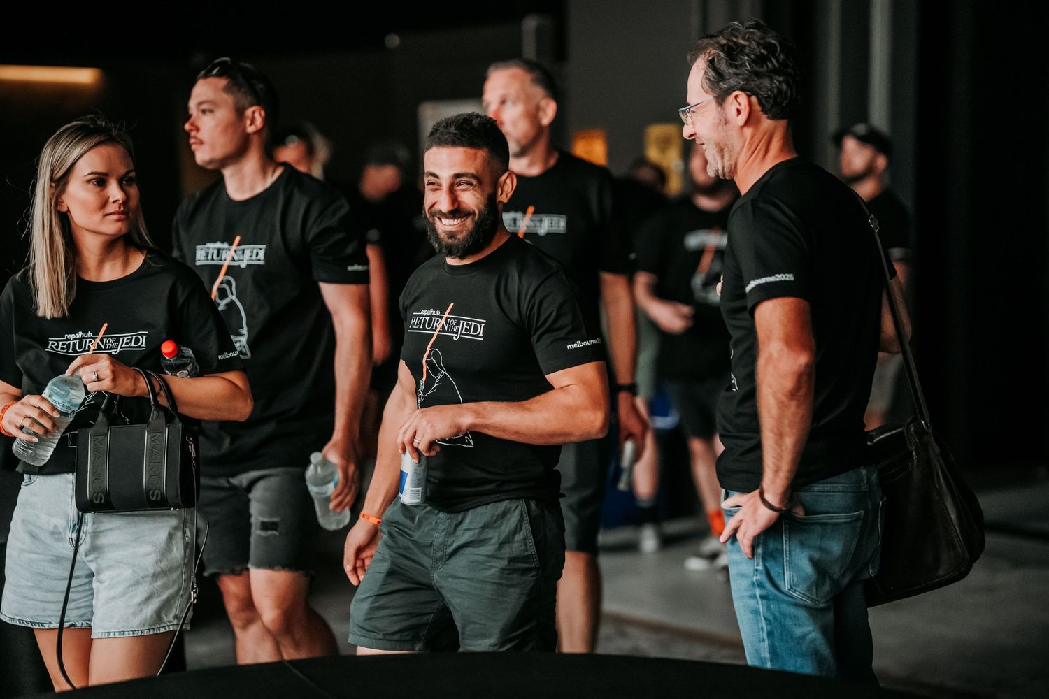 A group of people wearing black and gray athletic wear gather and socialize in a dimly lit indoor space.