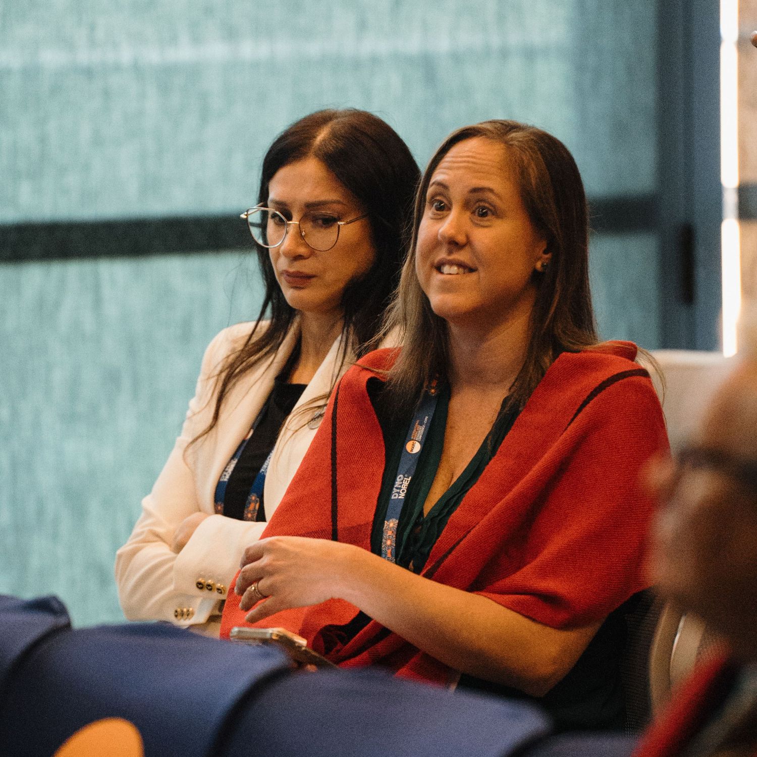 A group of conference attendees sitting in a row at a professional event, with one wearing a bright red jacket.